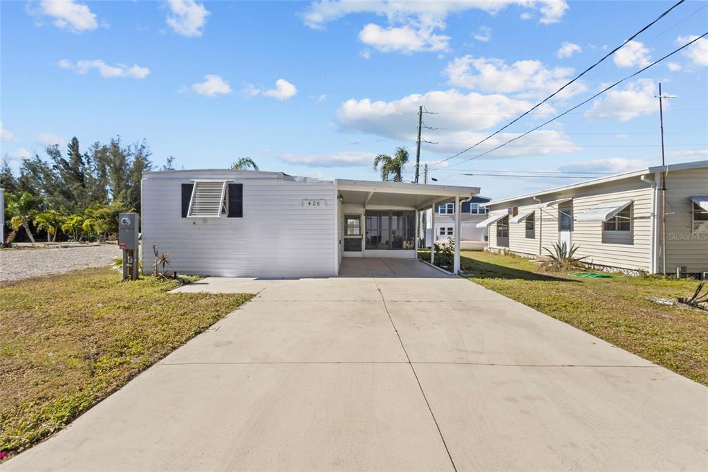 A white mobile home with a concrete driveway and an attached carport under a blue sky — 426 HATCHETT CREEK ROAD, VENICE, FL