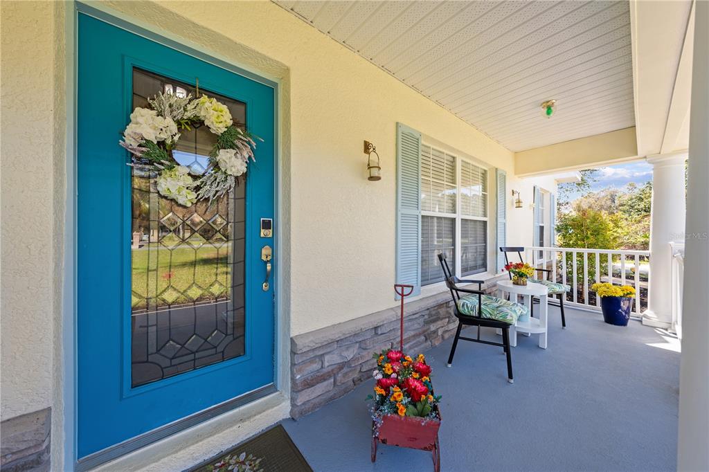 A covered front porch features a bright blue door, a seating area, and potted flowers — 6409 SHORELINE COURT, ST CLOUD, FL