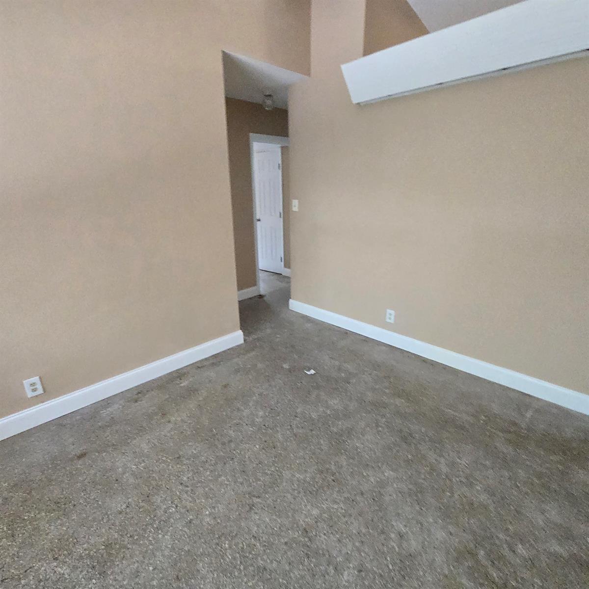 An empty room with tan walls, white trim, and gray carpet leads to a doorway — 830 SW 14th Street # 2, Pompano Beach FL 33060, POMPANO BEACH, FL