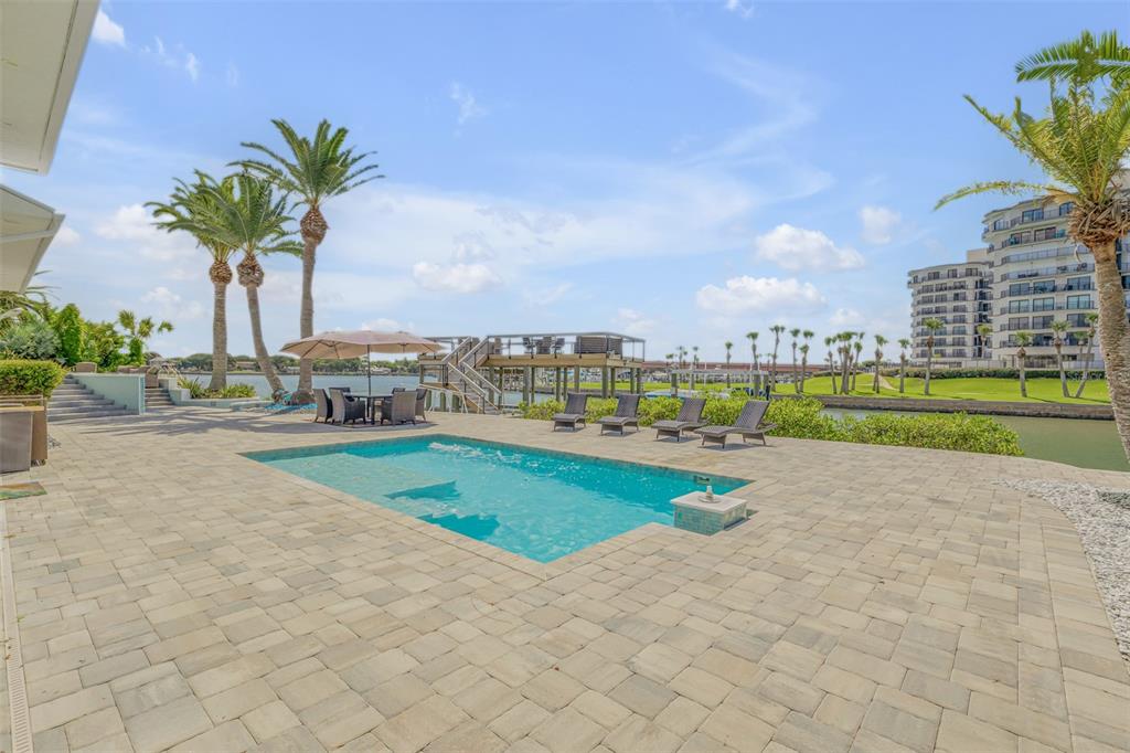 A swimming pool sits on a stone patio overlooking a canal with a wooden dock — 444 QUAY ASSISI COURT, NEW SMYRNA BEACH, FL