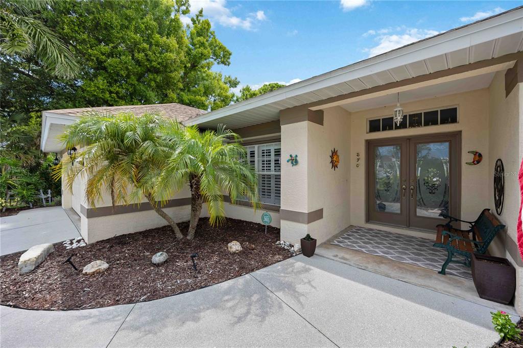 A beige house exterior features a double front door, a palm tree, and a concrete walkway — 230 E GREEN STREET, ENGLEWOOD, FL