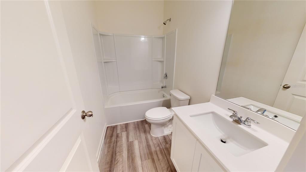 A bathroom features a white vanity, a toilet, and a tub-shower combo with wood-look flooring — 14554 ITALY AVENUE, DADE CITY, FL