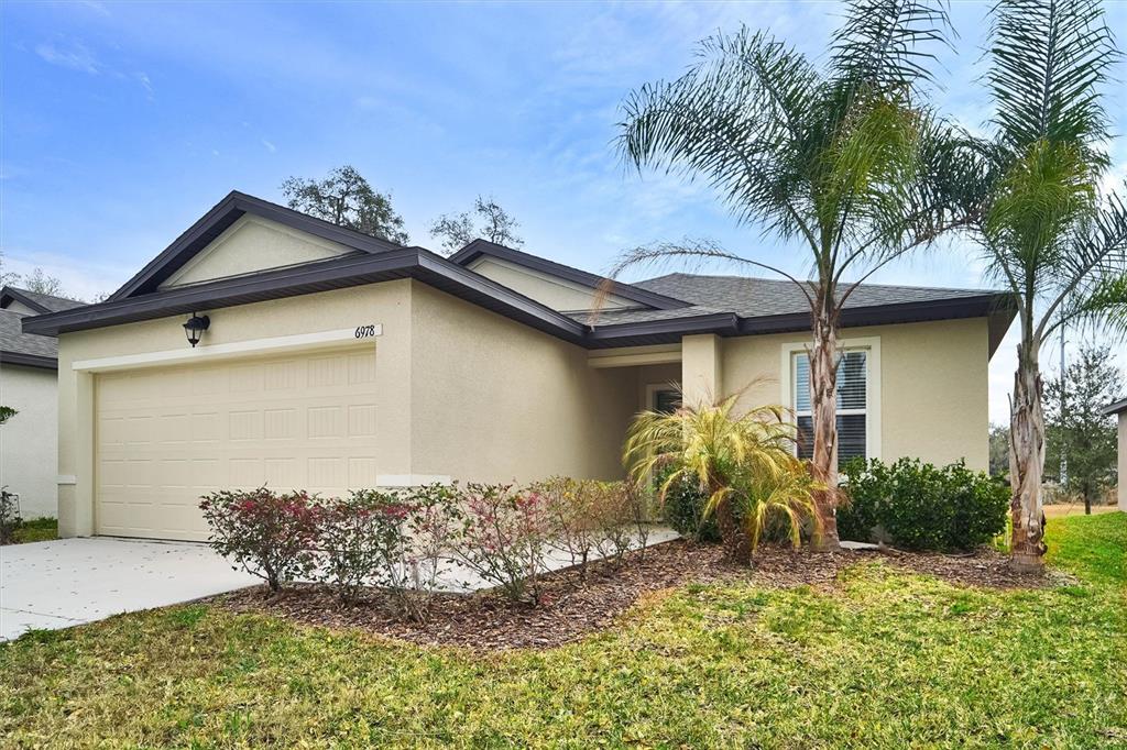 A single-story house with a beige stucco exterior, a two-car garage, and two palm trees — 6978 FABEN LANE, ZEPHYRHILLS, FL