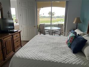 A bedroom with a bed, wooden dresser, television, and sliding glass doors leading to a balcony — 9712 SEA TURTLE TERRACE UNIT 102, BRADENTON, FL