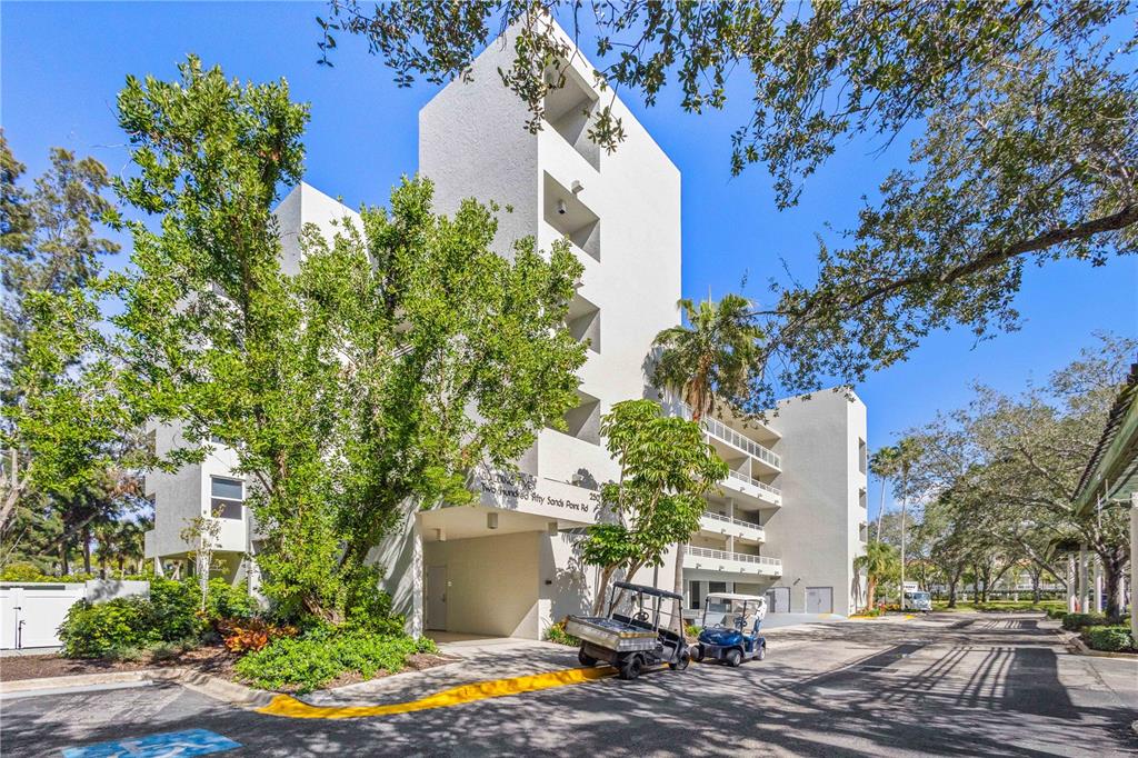 A multi-story white apartment building with balconies and golf carts parked in the driveway — 250 SANDS POINT ROAD UNIT 5106, LONGBOAT KEY, FL
