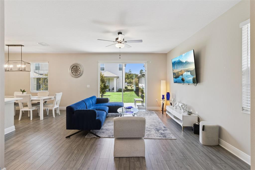 A living room with a blue sectional sofa, a wall-mounted television, and sliding glass doors — 7745 SOMERSWORTH DRIVE, KISSIMMEE, FL