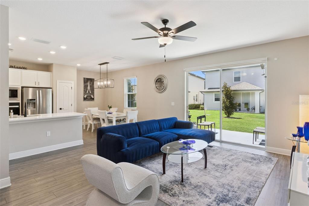 An open-concept living and dining area features a blue sectional sofa, wood-look flooring, and sliding doors — 7745 SOMERSWORTH DRIVE, KISSIMMEE, FL