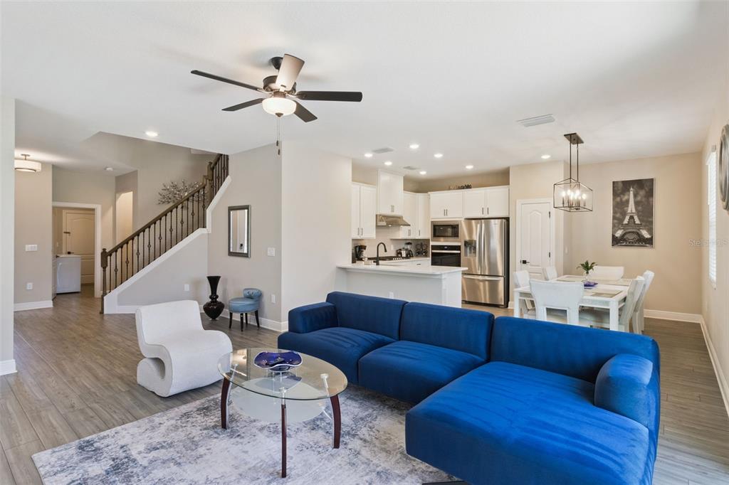 An open-concept living room and kitchen featuring a blue sectional sofa and white cabinetry — 7745 SOMERSWORTH DRIVE, KISSIMMEE, FL