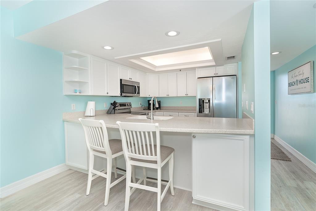 A kitchen features white cabinets, light countertops, a breakfast bar with two chairs, and light-blue walls — 7466 PALM ISLAND DRIVE UNIT 2911, PLACIDA, FL