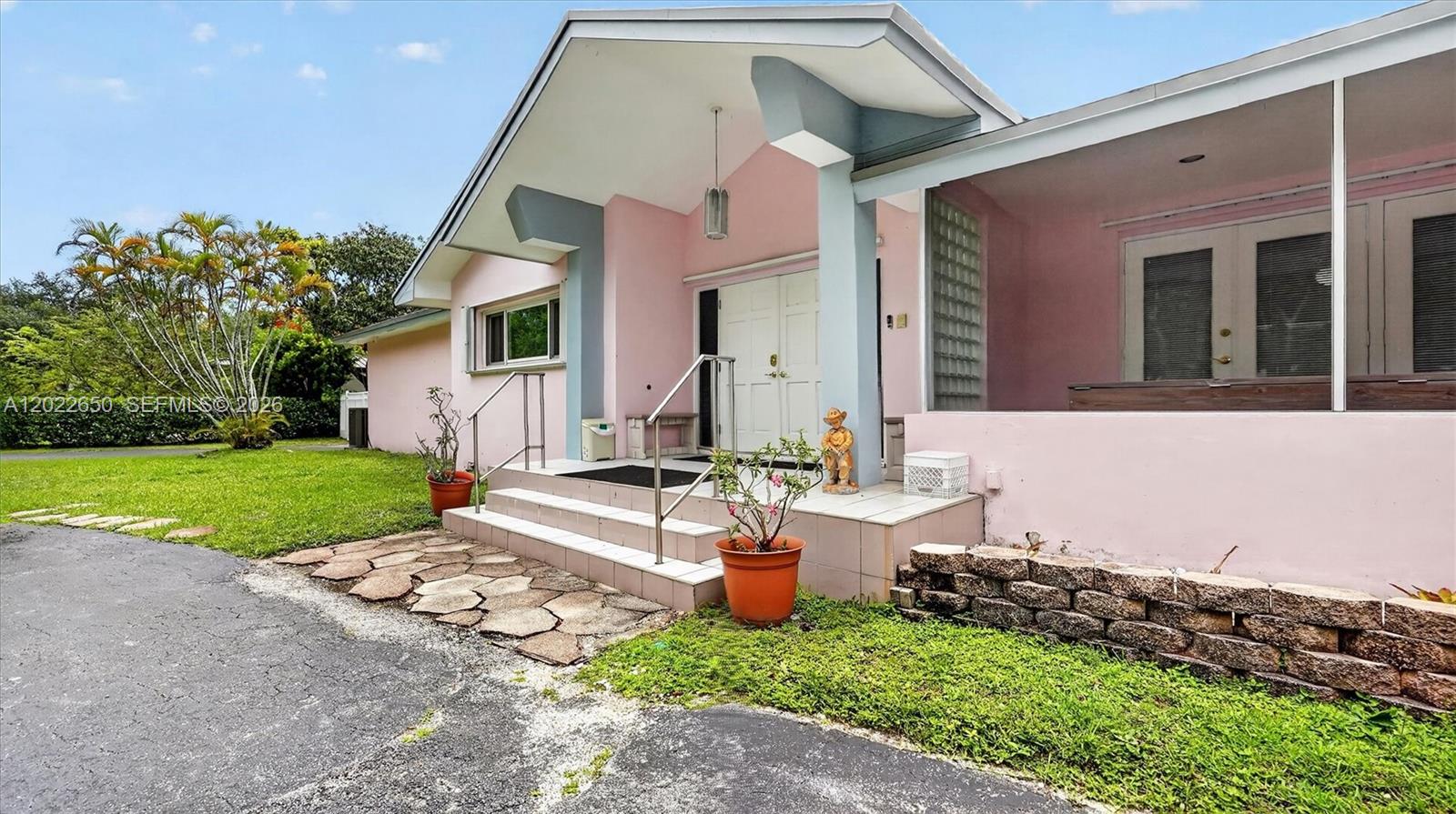 The exterior of a pink house features a covered porch, stone steps, and landscaping — 11651 SW 64th Ave, Pinecrest FL 33156, PINECREST, FL