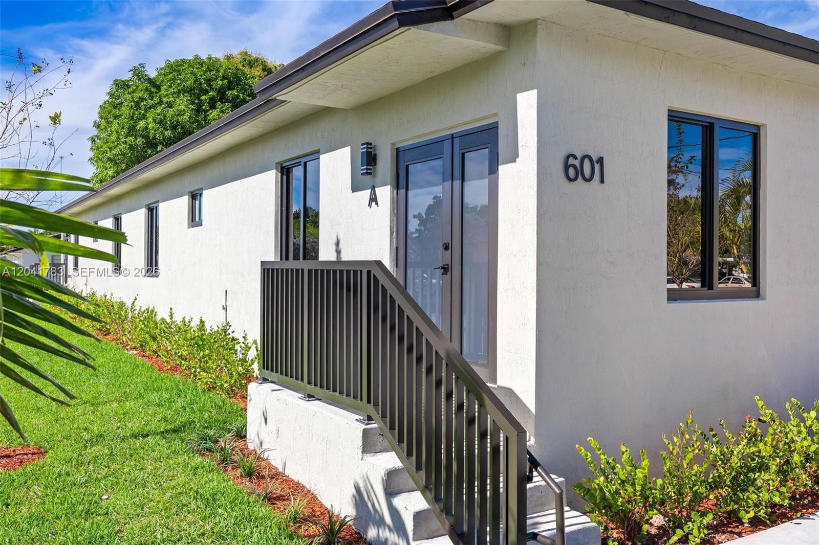 A white exterior wall features a black-framed glass door, a metal railing, and address numbers — 601 NW 3rd Ave, Hallandale Beach FL 33009, HALLANDALE BEACH, FL
