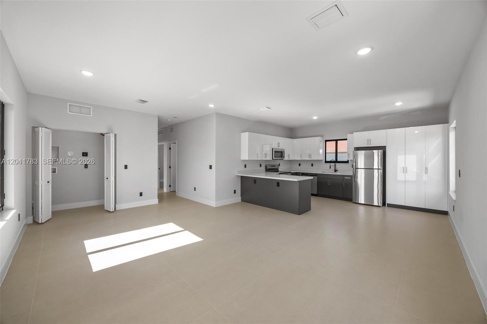A modern kitchen with white and gray cabinetry opens into a spacious, tiled living area — 601 NW 3rd Ave, Hallandale Beach FL 33009, HALLANDALE BEACH, FL