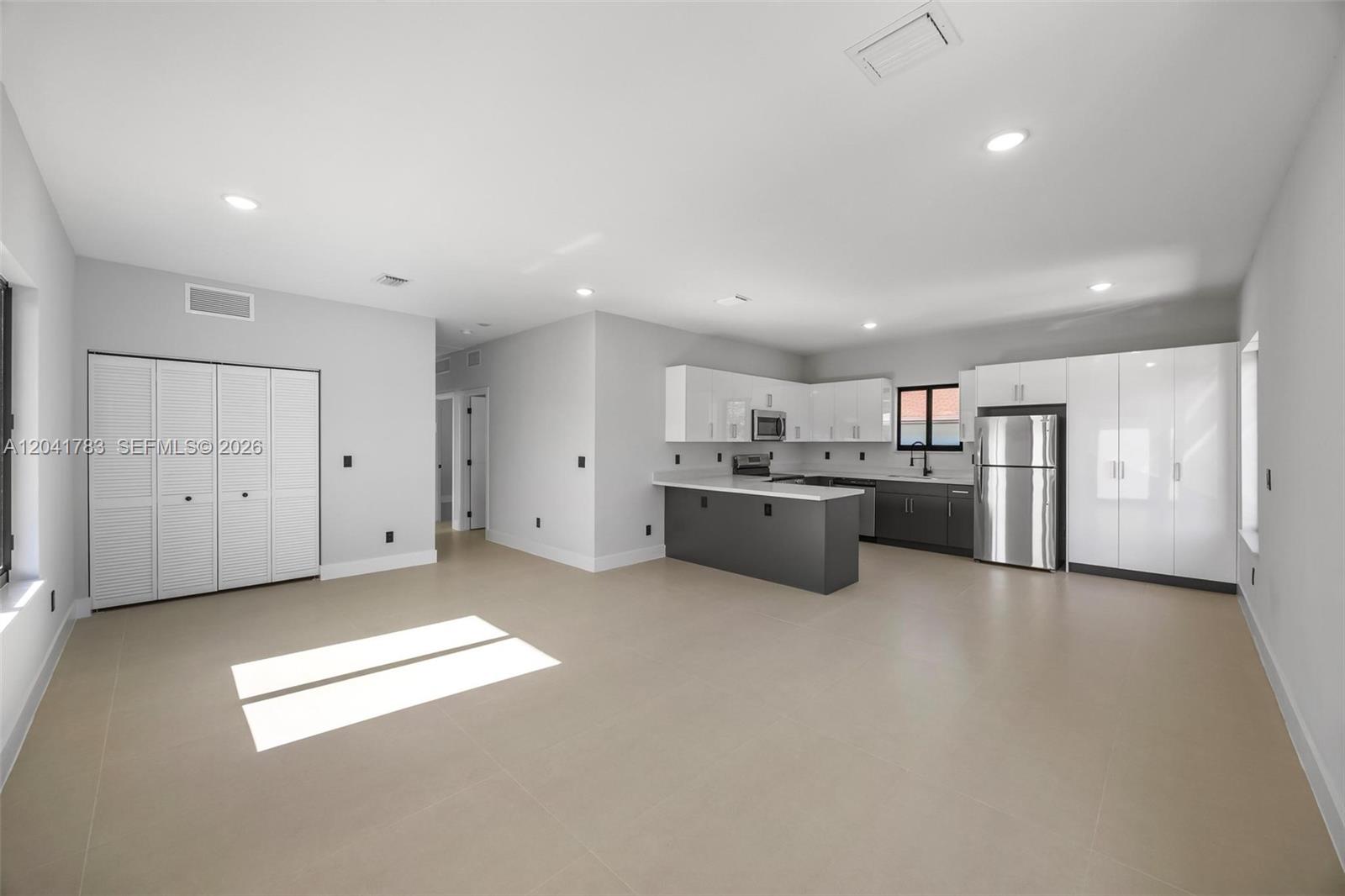 A modern open-concept kitchen features white and dark gray cabinetry, stainless steel appliances, and tile flooring — 601 NW 3rd Ave, Hallandale Beach FL 33009, HALLANDALE BEACH, FL