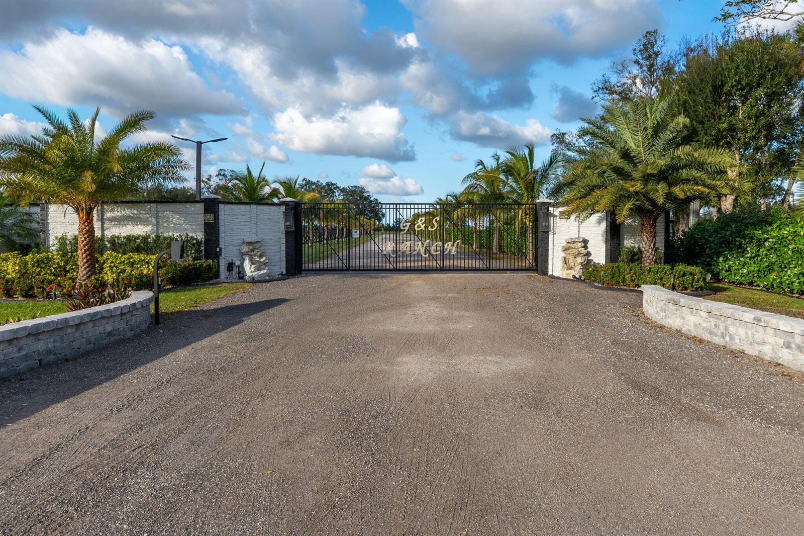 A gravel driveway leads to a gated entrance with a stone wall and palm trees — 16200 Orange Avenue, Fort Pierce FL 34945, FORT PIERCE, FL