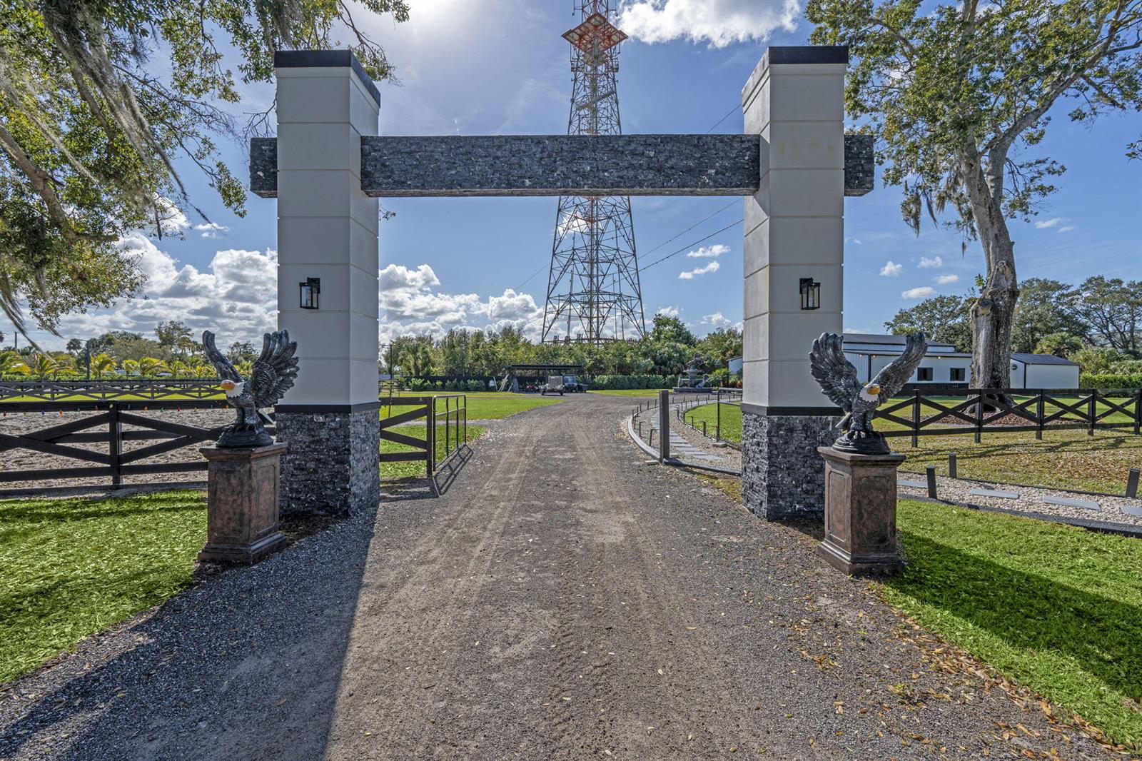 A gravel driveway leads through a stone-pillared gate topped with eagle statues toward a tower — 16200 Orange Avenue, Fort Pierce FL 34945, FORT PIERCE, FL