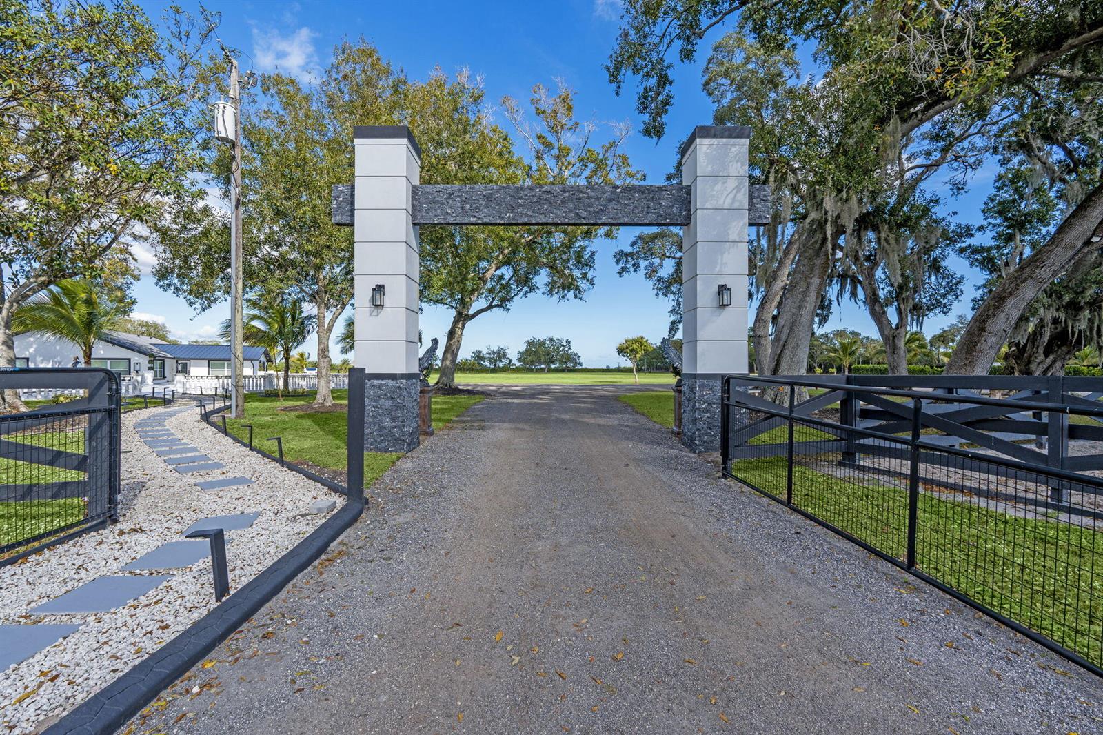 A gravel driveway leads through a modern stone and concrete gate entrance to a property — 16200 Orange Avenue, Fort Pierce FL 34945, FORT PIERCE, FL