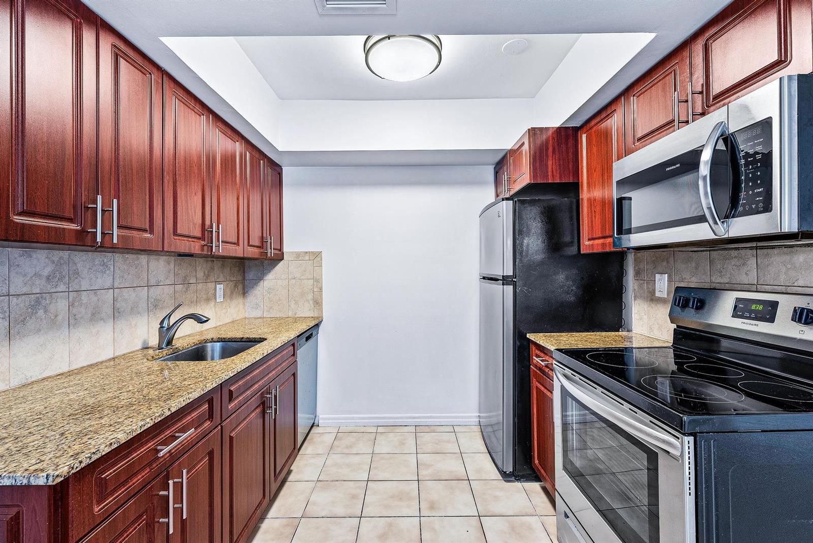 A galley kitchen features cherry wood cabinets, granite countertops, stainless steel appliances, and tile flooring — 242 NE 12th Street # 2, Delray Beach FL 33444, DELRAY BEACH, FL