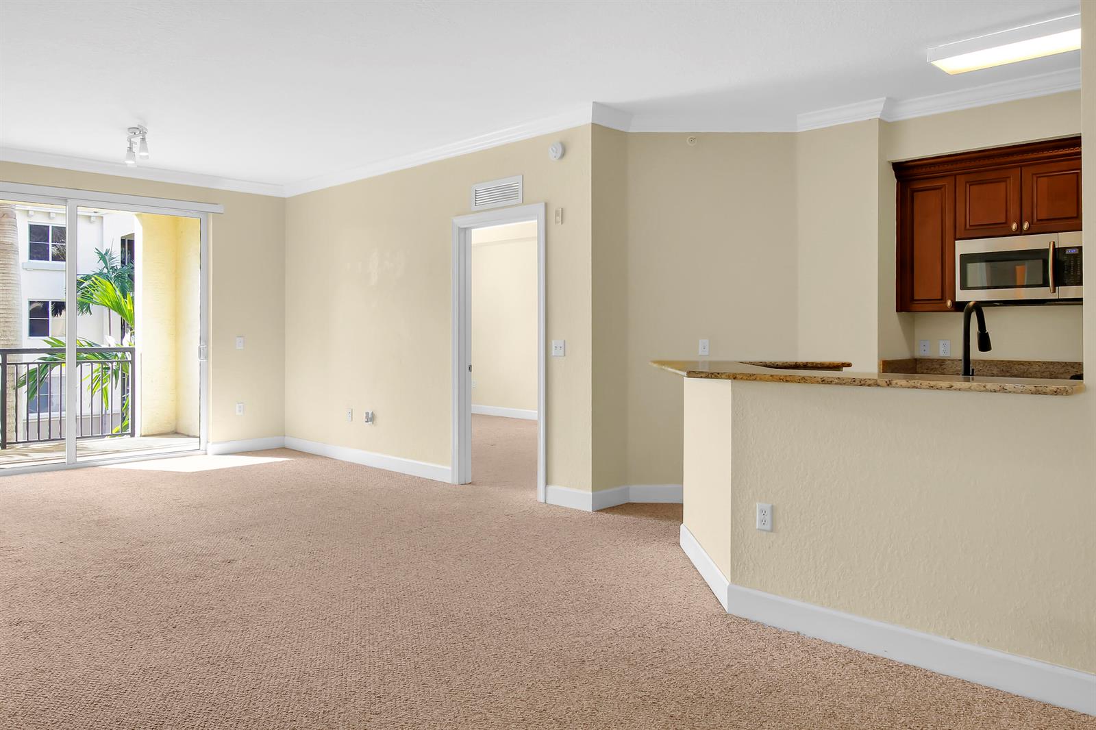 An interior view shows a carpeted living area with a balcony and an open kitchen — 1690 Renaissance Commons Boulevard # 1212, Boynton Beach FL 33426, BOYNTON BEACH, FL