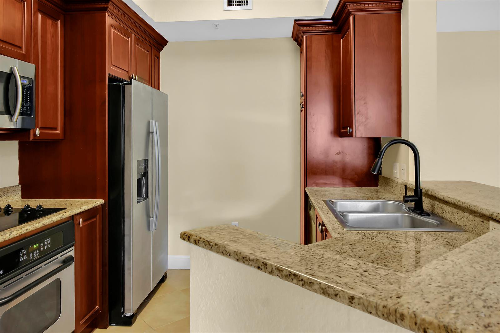 A kitchen features cherry wood cabinets, granite countertops, stainless steel appliances, and a double sink — 1690 Renaissance Commons Boulevard # 1212, Boynton Beach FL 33426, BOYNTON BEACH, FL