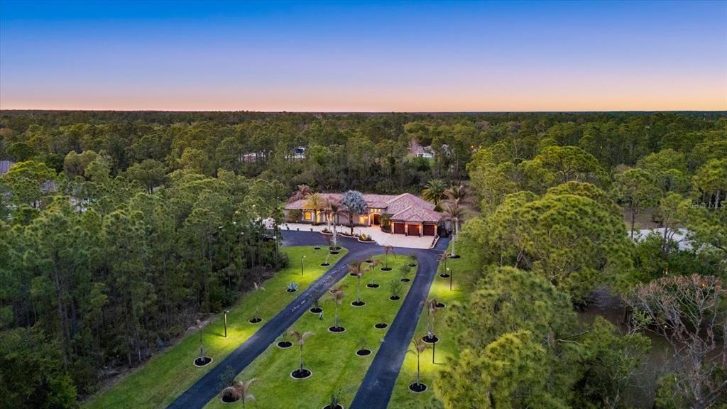 An aerial view shows a house with a long driveway surrounded by trees at sunset — 3604 TROPICAIRE BOULEVARD, NORTH PORT, FL