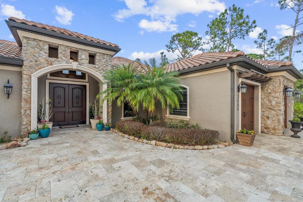 The exterior of a house features a stone facade, tile roof, and a paved driveway — 3604 TROPICAIRE BOULEVARD, NORTH PORT, FL