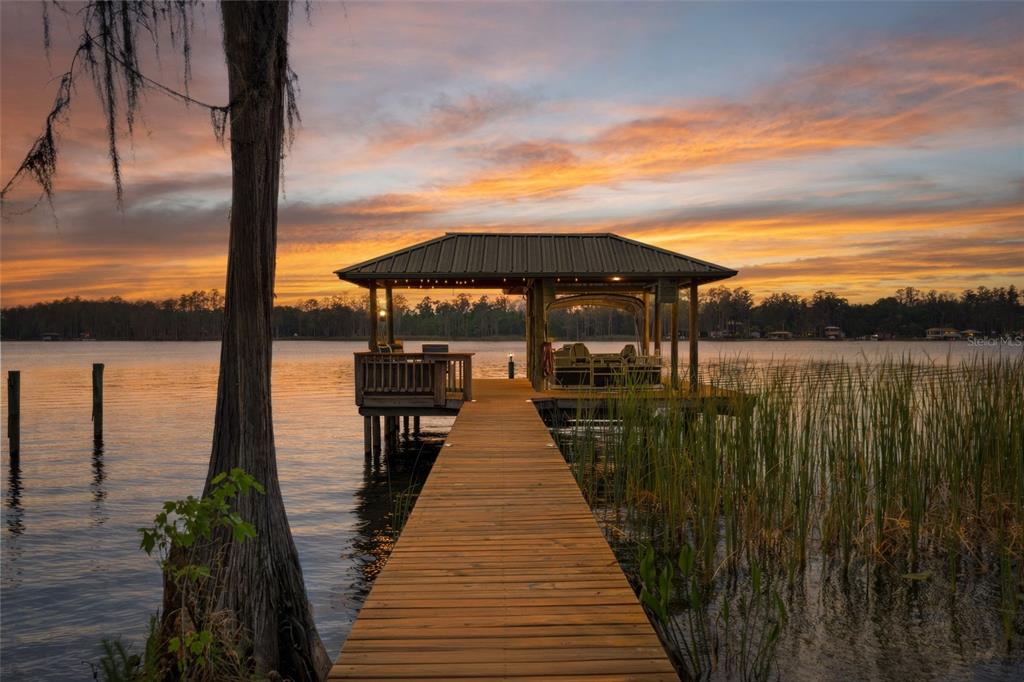 A wooden dock leads to a covered boat slip on a lake at sunset — 21133 MARSH HAWK DRIVE, LAND O LAKES, FL