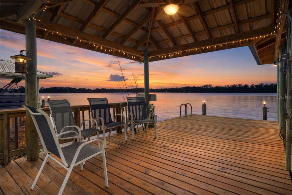 A wooden boat dock with a covered seating area overlooks a lake at sunset — 21133 MARSH HAWK DRIVE, LAND O LAKES, FL
