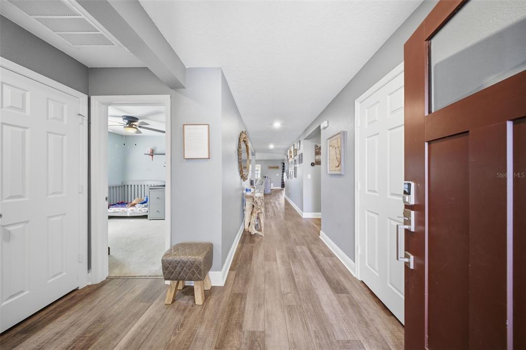 A hallway with wood-look flooring leads from a front door past a bedroom entrance — 232 LAKE LUCERNE WAY, WINTER HAVEN, FL