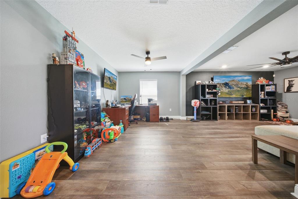 A spacious room features wood-look flooring, a desk area, shelving units, and children's toys — 232 LAKE LUCERNE WAY, WINTER HAVEN, FL