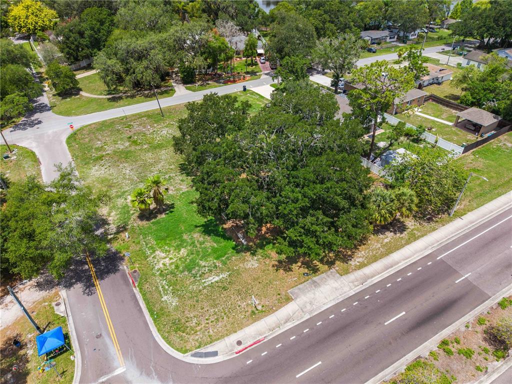 An aerial view shows a vacant, grassy corner lot with large trees and paved roads — 7514 N 40TH STREET, TAMPA, FL
