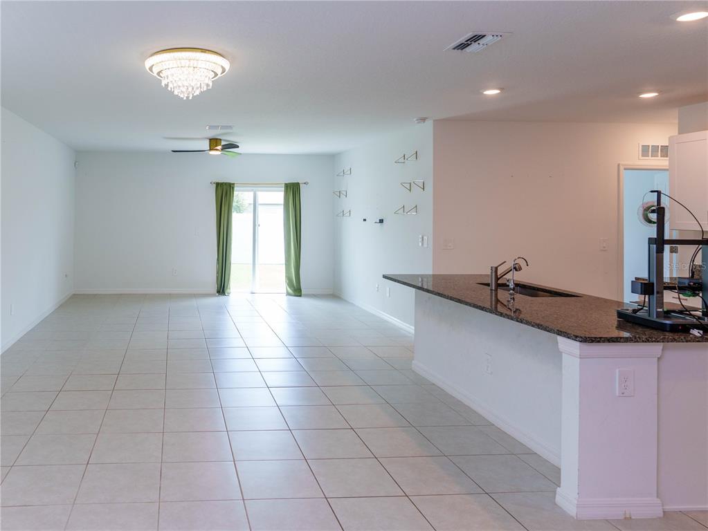 An open-concept living area features tile flooring, a kitchen island with granite countertops, and sliding doors — 13693 NEWBRIDGE STREET, SPRING HILL, FL