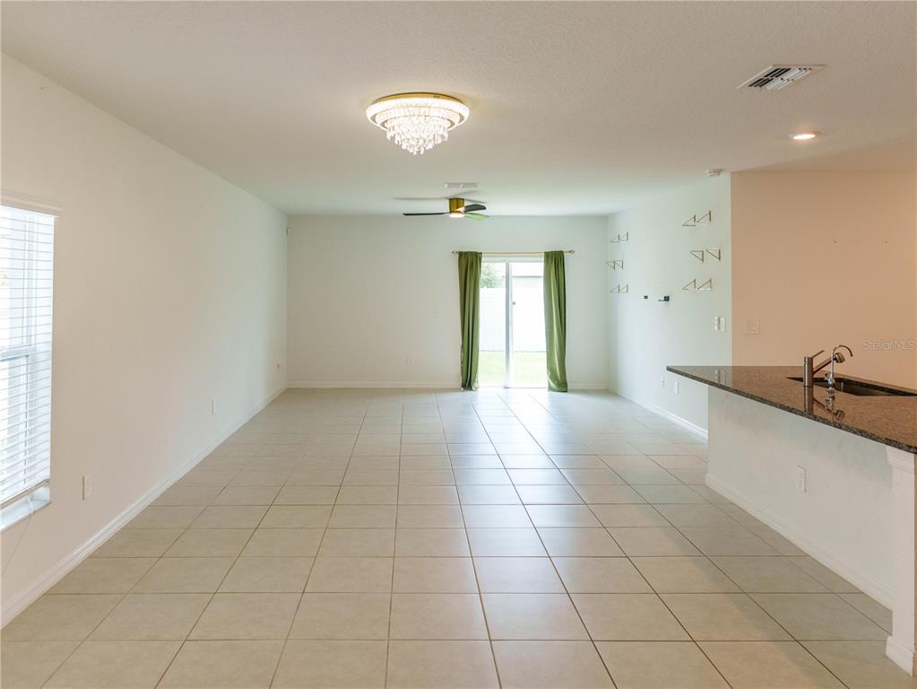 An open-concept living area features tile flooring, a crystal chandelier, and a granite kitchen island — 13693 NEWBRIDGE STREET, SPRING HILL, FL