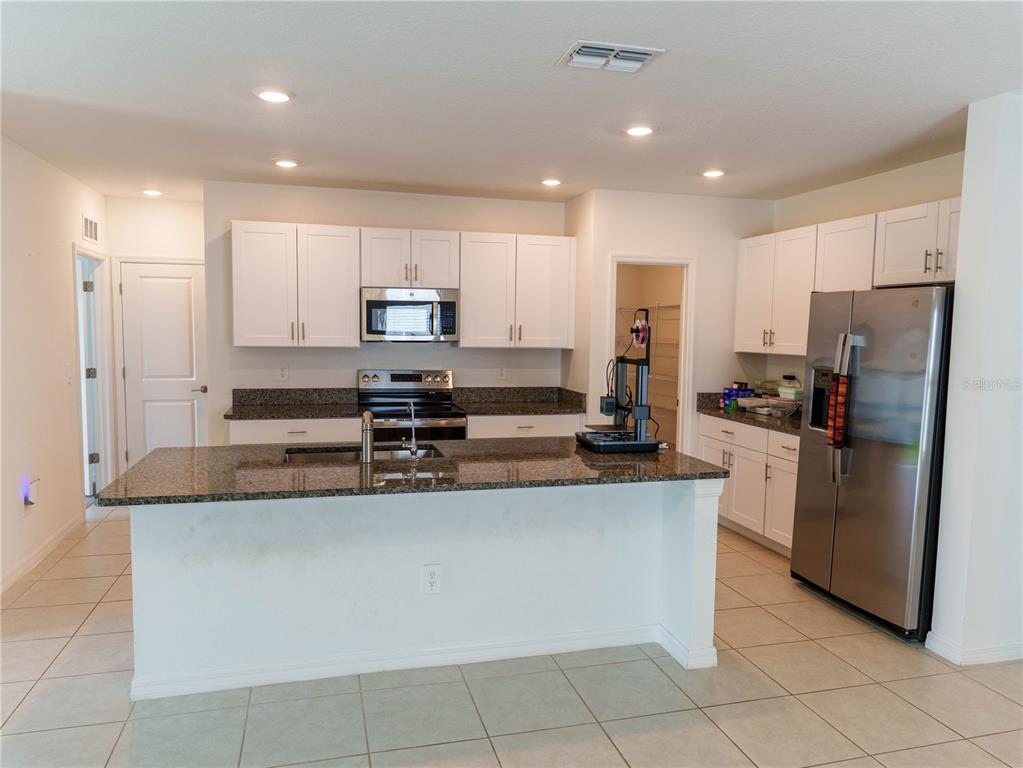 A kitchen features white cabinets, granite countertops, a center island, and stainless steel appliances — 13693 NEWBRIDGE STREET, SPRING HILL, FL