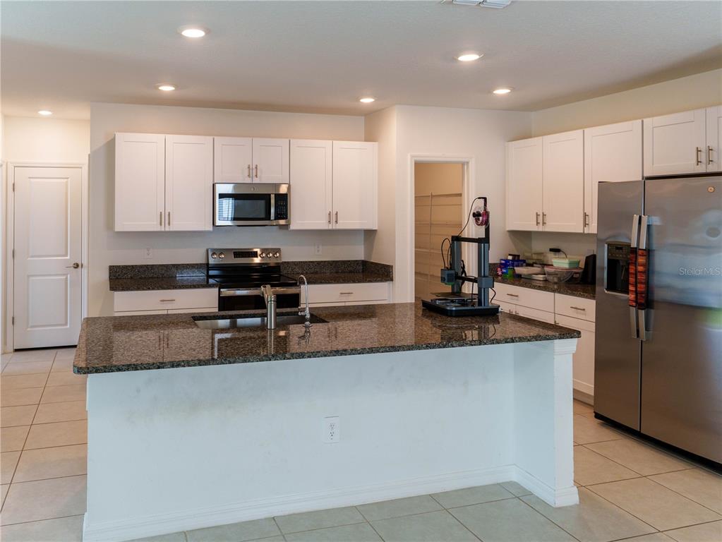 A kitchen features white cabinets, granite countertops, a center island, and stainless steel appliances — 13693 NEWBRIDGE STREET, SPRING HILL, FL