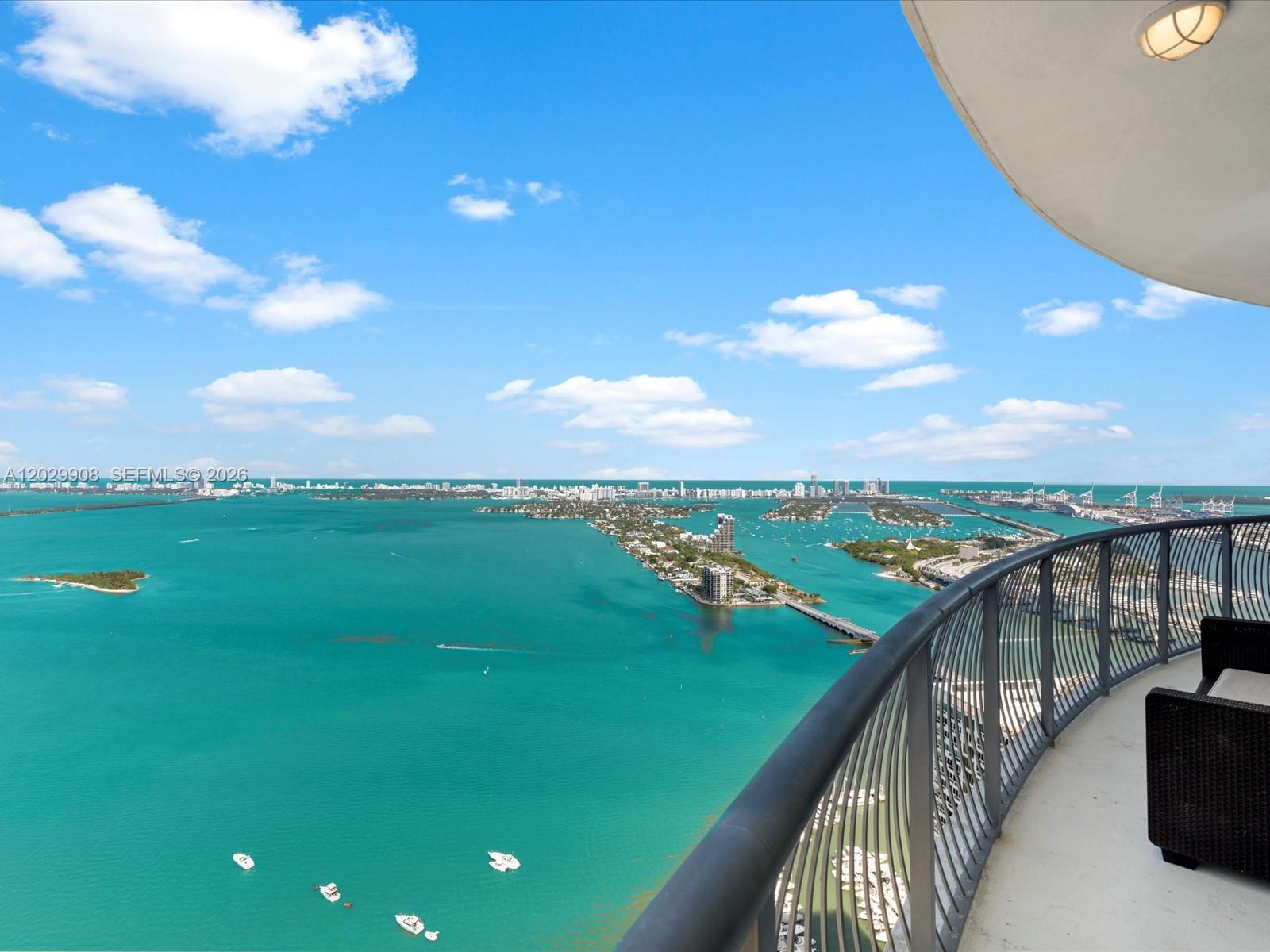 A high-rise balcony overlooks a turquoise bay with islands and a distant city skyline — 1750 N Bayshore Dr # 5601, Miami FL 33132, MIAMI, FL
