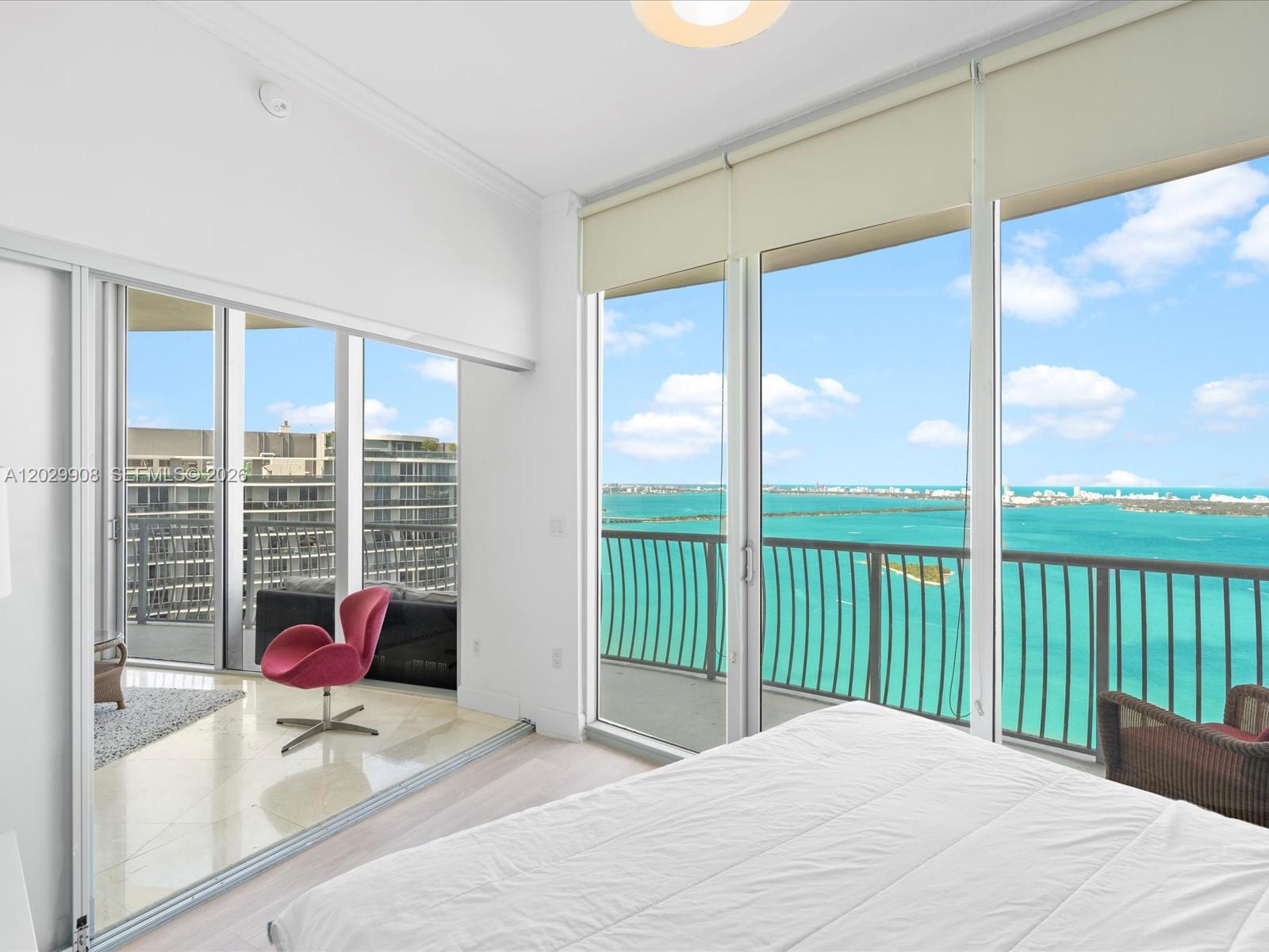 A bedroom features floor-to-ceiling windows with a balcony overlooking a bright blue bay — 1750 N Bayshore Dr # 5601, Miami FL 33132, MIAMI, FL