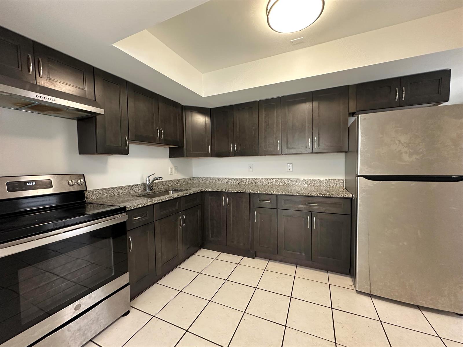 A kitchen features dark wood cabinets, granite countertops, stainless steel appliances, and tiled flooring — 4606 SE Binnacle Way # 1, Stuart FL 34997, STUART, FL