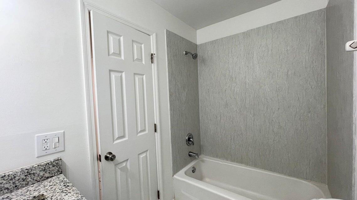 A bathroom features a white bathtub with a gray textured surround and a white door — 4606 SE Binnacle Way # 1, Stuart FL 34997, STUART, FL