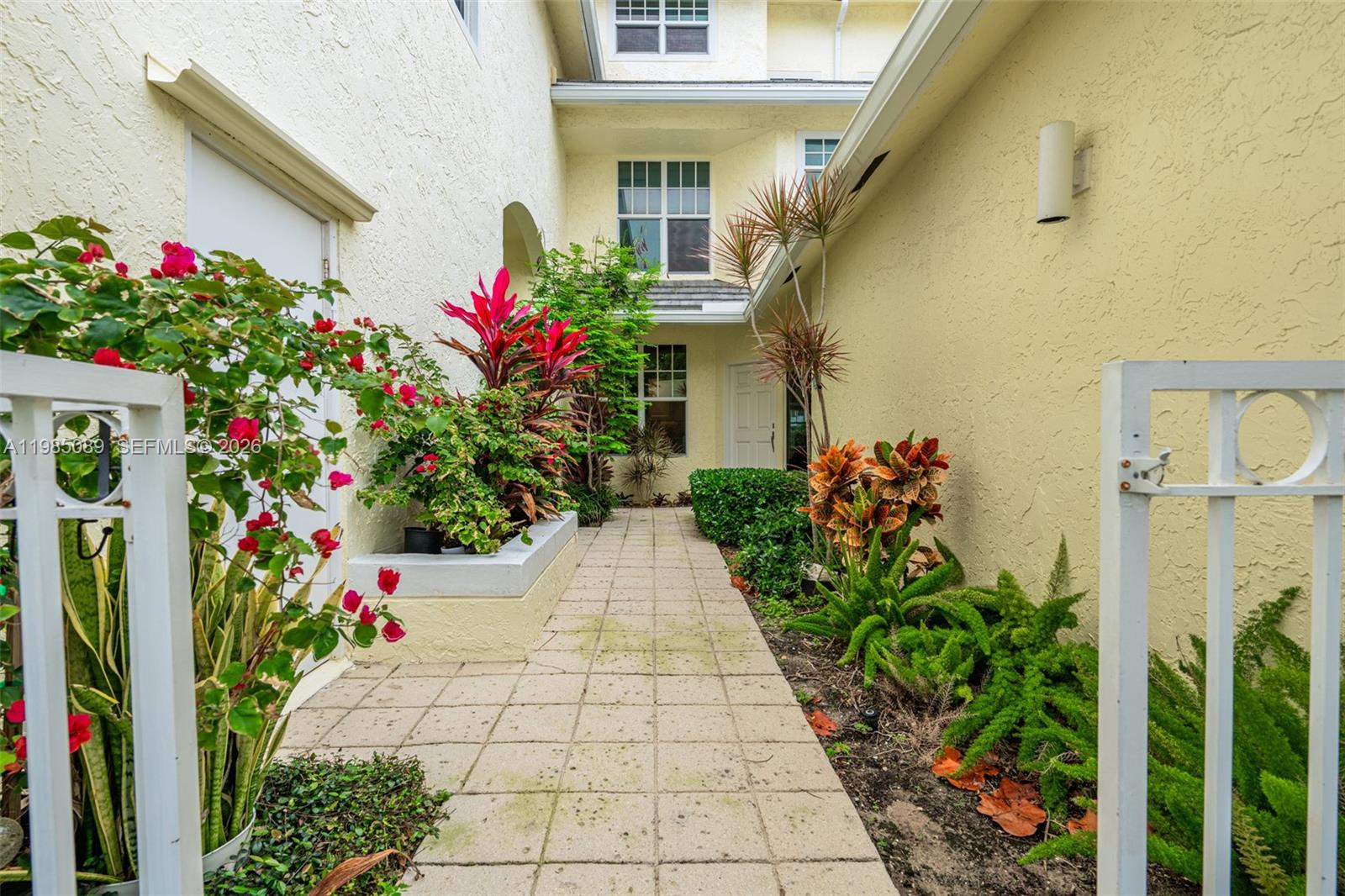 A paved walkway leads to a building entrance surrounded by lush tropical landscaping and flowers — 1404 Mainsail Cir # 1404, Jupiter FL 33477, JUPITER, FL
