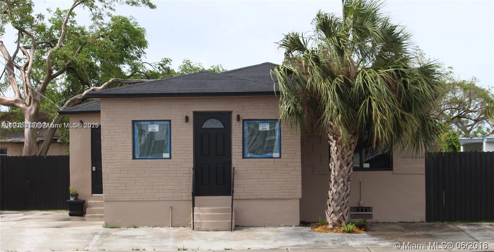 A single-story house with tan textured siding, a black front door, and a palm tree — 107 W Pembroke Rd, Hallandale Beach FL 33009, HALLANDALE BEACH, FL