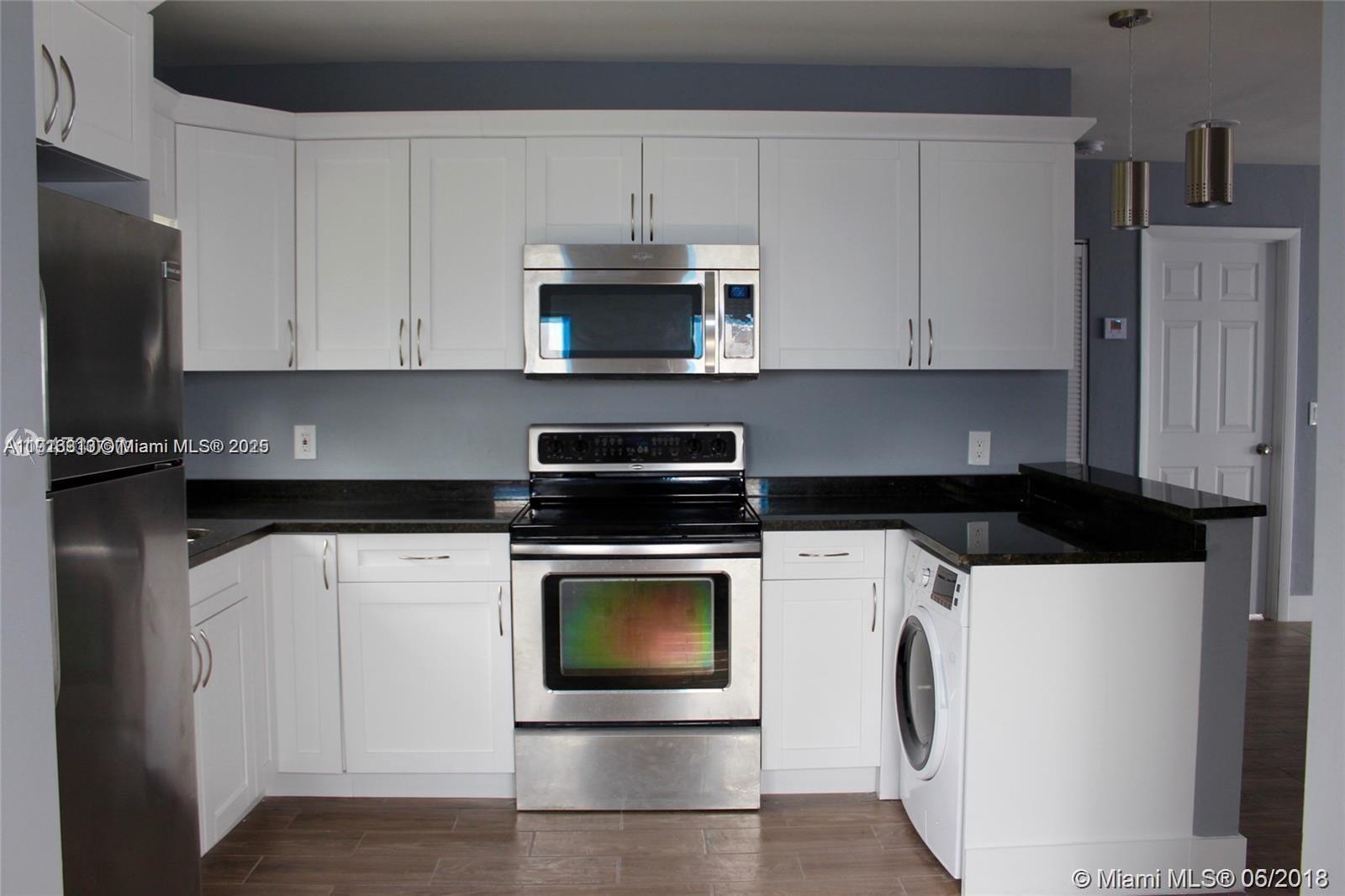 A kitchen features white cabinets, stainless steel appliances, a black countertop, and a built-in washer — 107 W Pembroke Rd, Hallandale Beach FL 33009, HALLANDALE BEACH, FL