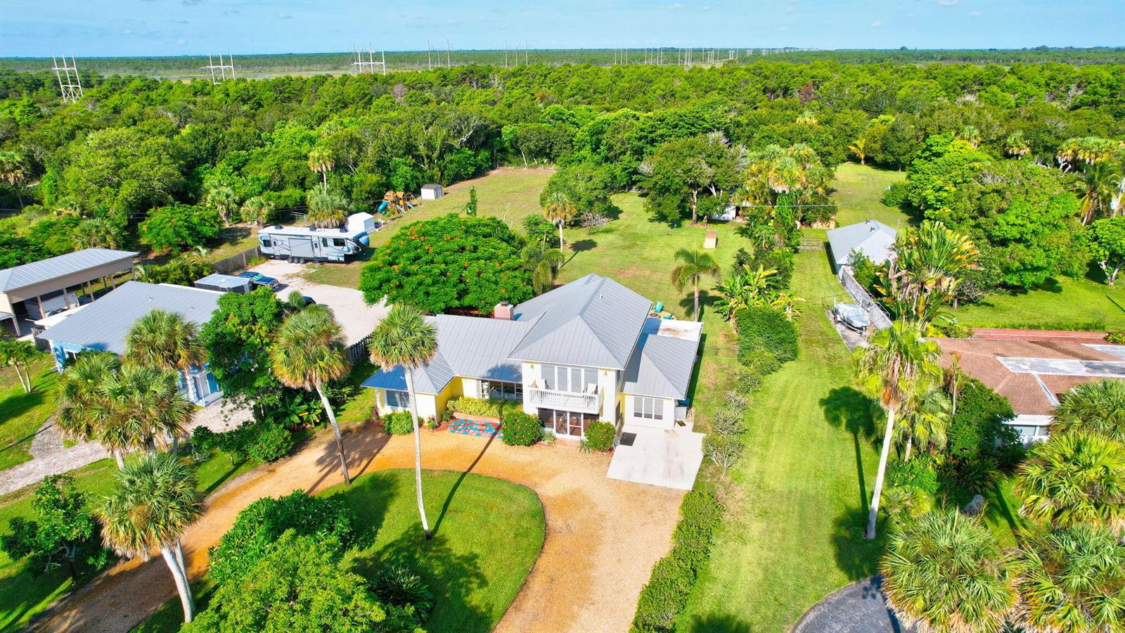 An aerial view shows a yellow house with a metal roof surrounded by lush greenery — 7501 S Indian River Drive, Fort Pierce FL 34982, FORT PIERCE, FL
