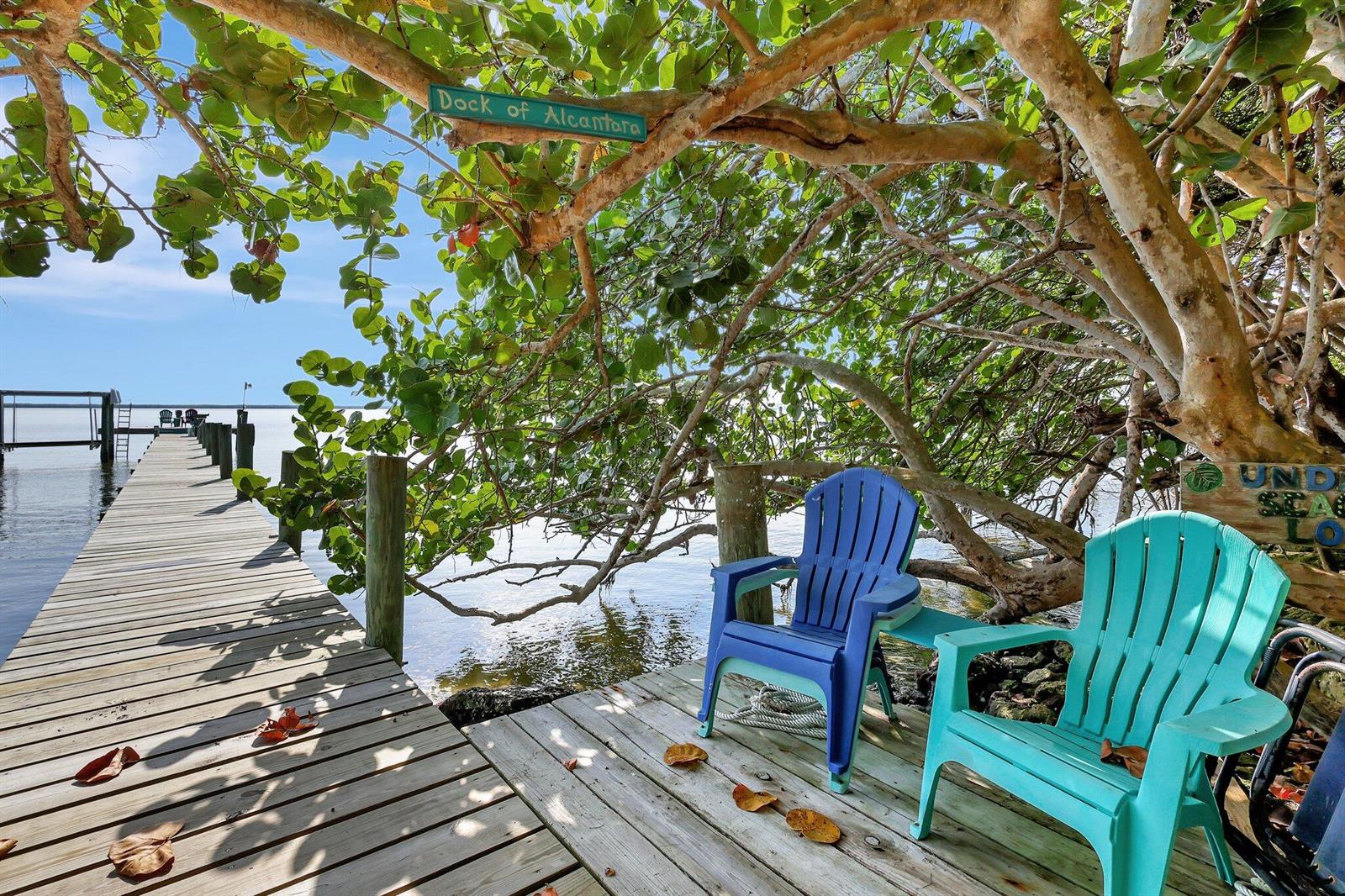 A wooden dock extends over the water with two colorful chairs under a large tree — 7501 S Indian River Drive, Fort Pierce FL 34982, FORT PIERCE, FL