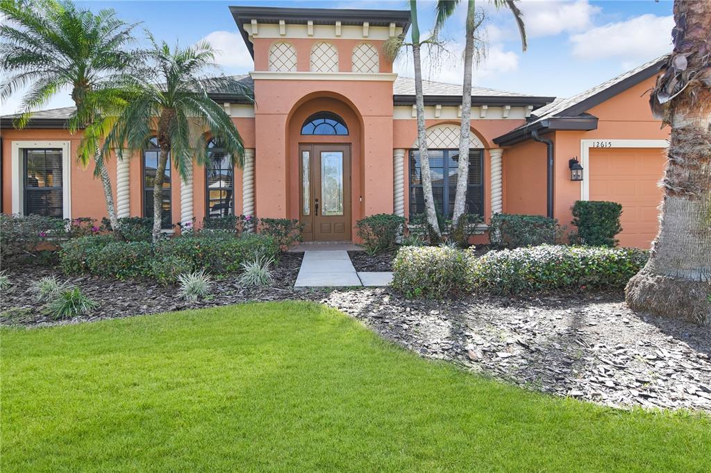 A single-story peach-colored house features a central arched entryway, spiral columns, and a front lawn — 12615 20TH STREET E, PARRISH, FL