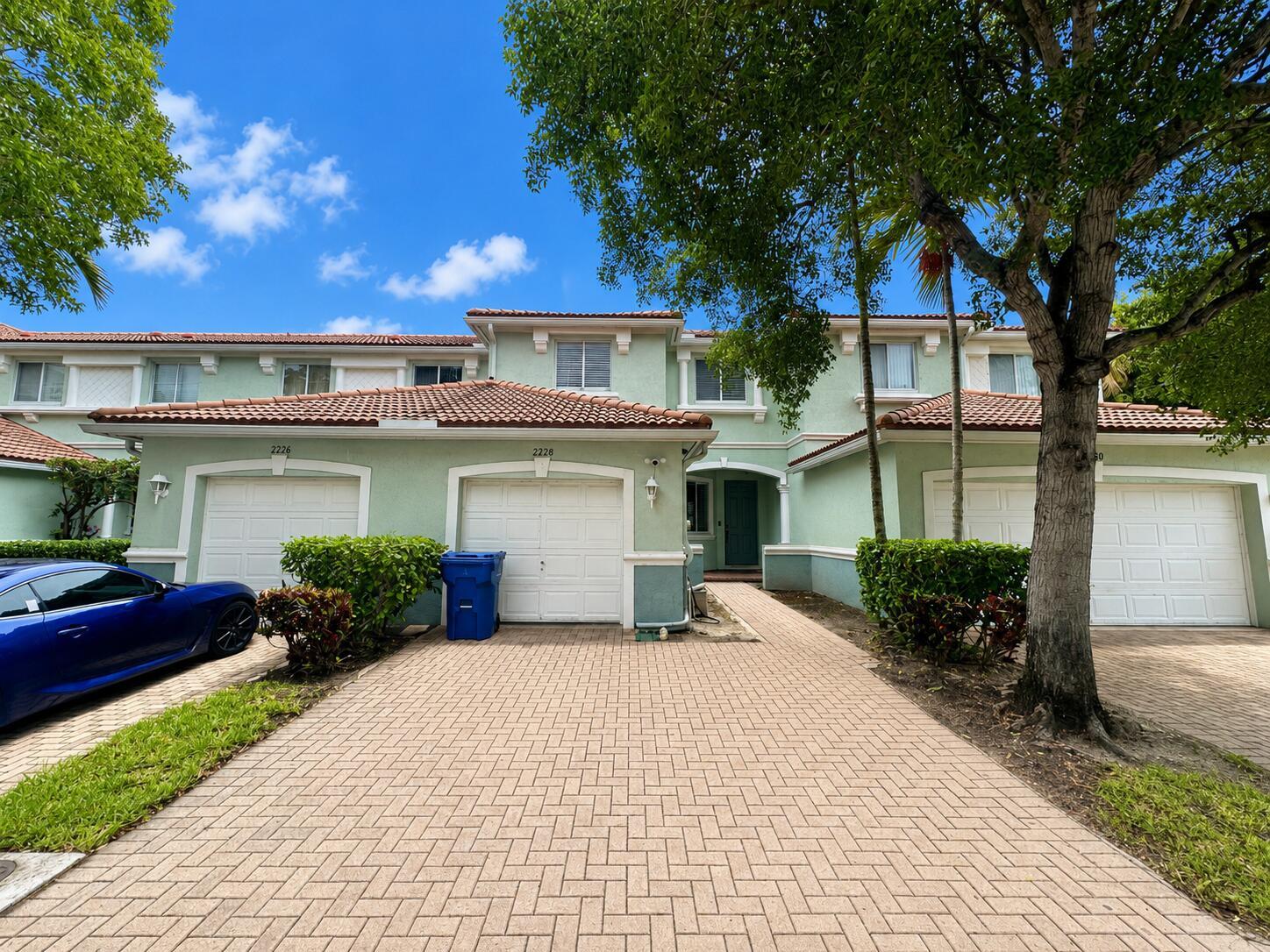 A two-story townhouse with a light green exterior, tiled roof, and a paved driveway — 2228 Oakmont Drive, Riviera Beach FL 33404, RIVIERA BEACH, FL