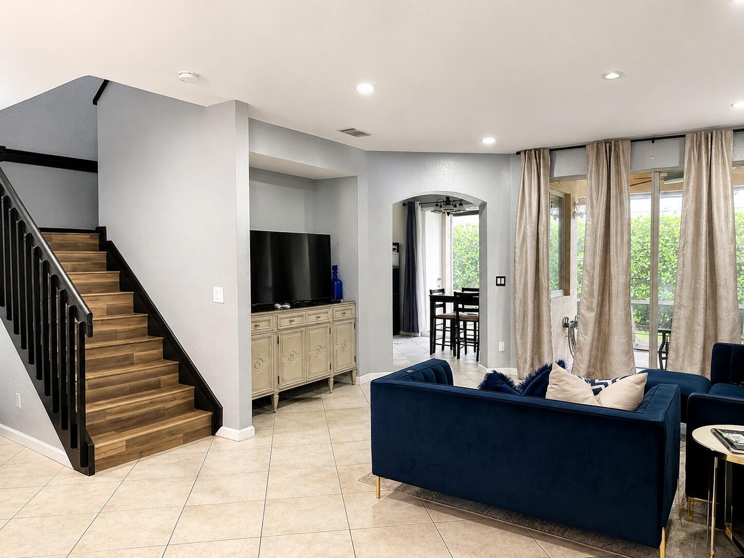 A living room features a blue velvet sofa, a wooden staircase, and a media console — 2228 Oakmont Drive, Riviera Beach FL 33404, RIVIERA BEACH, FL