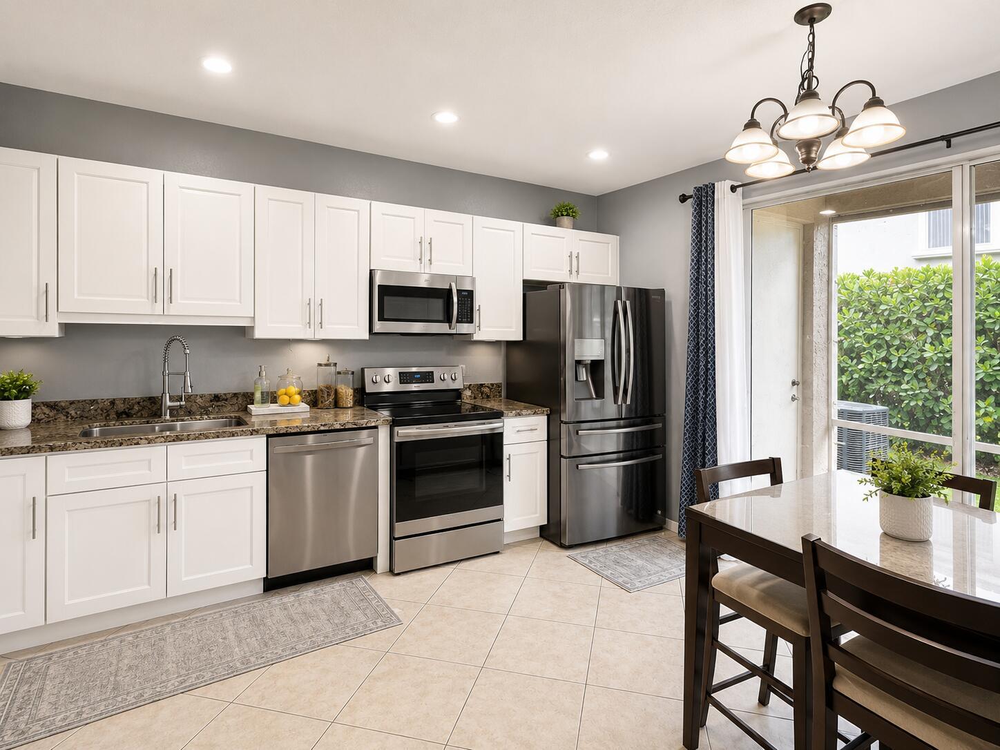 A kitchen with white cabinets, stainless steel appliances, granite countertops, and a dining area — 2228 Oakmont Drive, Riviera Beach FL 33404, RIVIERA BEACH, FL