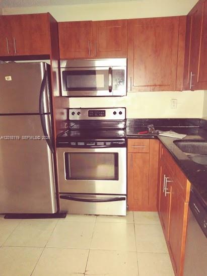 A kitchen features wooden cabinets, stainless steel appliances, and dark countertops over light tile flooring — 492 NW 165 St Rd # C516, Miami FL 33169, MIAMI, FL