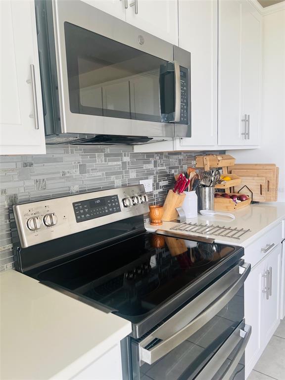 A kitchen features white cabinets, stainless steel appliances, and a gray tiled backsplash — 1120 SUGARWOOD STREET, DAVENPORT, FL