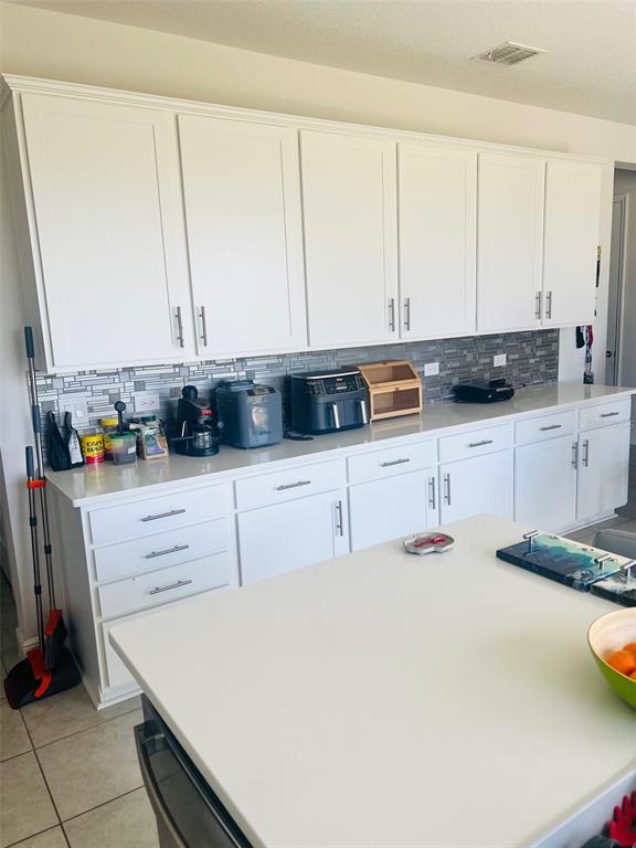 A kitchen features white cabinets, a light-colored countertop, and a gray tiled backsplash — 1120 SUGARWOOD STREET, DAVENPORT, FL